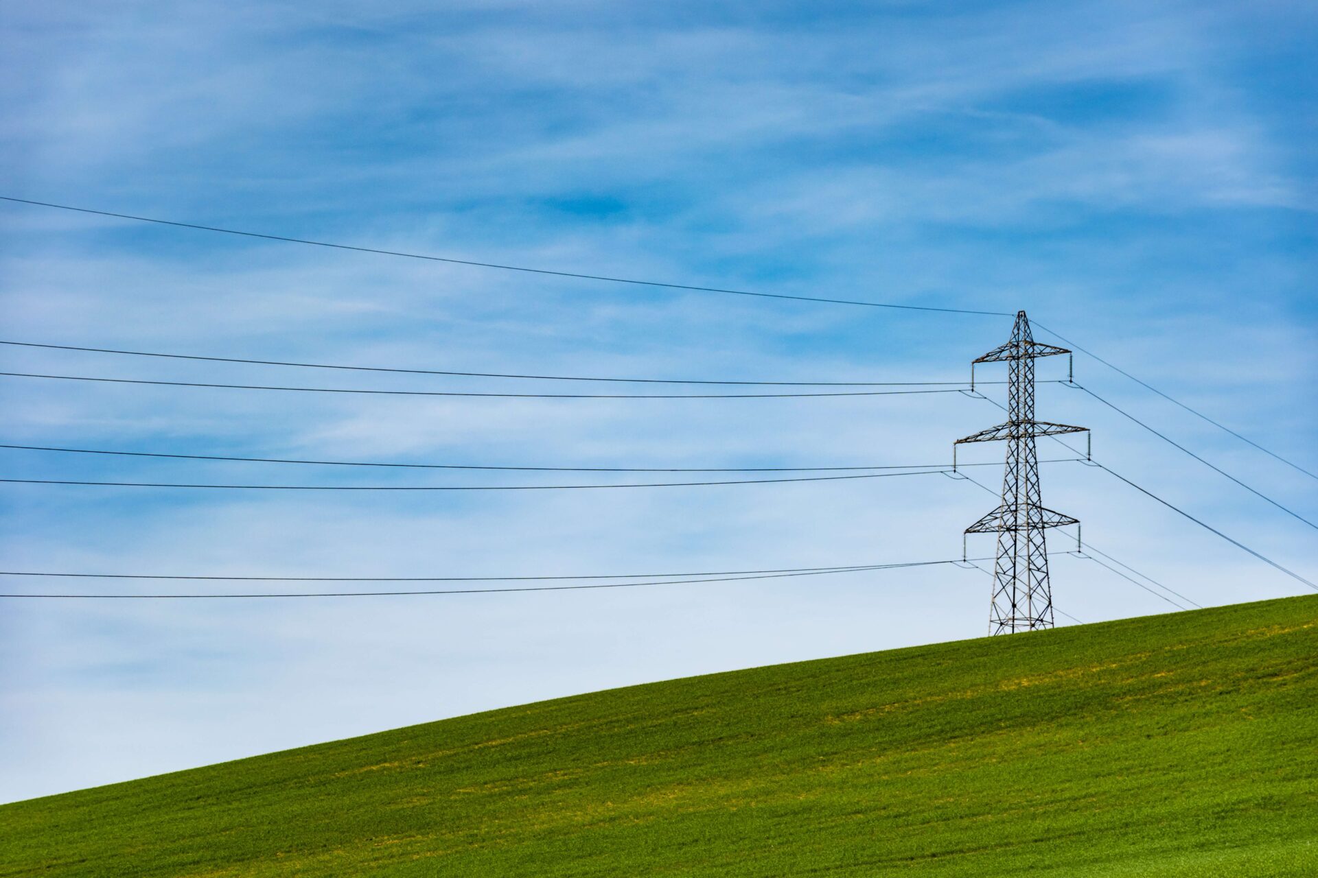 Transmission lines pictured on green hills with blue sky in the background.